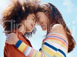 Close up of two young mixed race female couple embracing each other and smiling outside on a sunny day. A Beautiful gay hispanic woman with a cool afro hair style showing affection by hugging her girlfriend while on a date