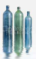 Three glass bottles on white surface with water effect. Old colorful vintage wine bottles arranged against a copy space background with reflections. Side view of unused containers in descending order