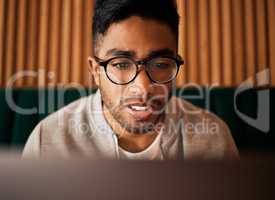 .. Closeup of geeky young indian man wearing glasses while reading something interesting and sitting inside. Man wearing glasses while reading online. Dedicated male student doing research in cafe.