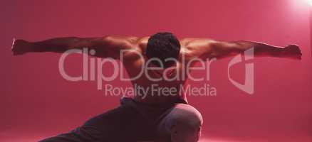 One strong indian man stretching arms while crouching against a red studio background. Fierce muscular and topless man with toned body looking ready to fight or demonstrate powerful martial arts moves