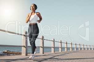 Full length of fit young female athlete in sportswear wearing wireless headphones and listening to music while out for a run along the promenade. Exercise is good for you health and wellbeing