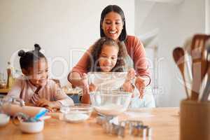 Females only, happy mixed race family of three cooking in a messy kitchen together. Loving black single parent bonding with her daughters while teaching them domestic skills at home