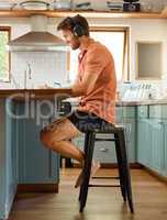 Fullbody of a young happy caucasian businessman wearing headphones and using a laptop at home alone. One joyful male businessperson smiling while working in the kitchen at home