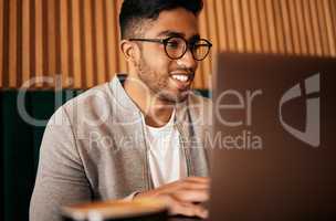 .. Handsome indian man with glasses sitting alone and using laptop in cafe. Man using wifi to browse the internet or doing freelance work in a cafe. Male student doing research on internet.