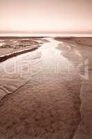 A golden sunset over rippling low tide waters on the west coast of Jutland in Loekken, Denmark. Beautiful and magical empty beach at dusk. Clouds over the ocean and sea in the evening with copy space