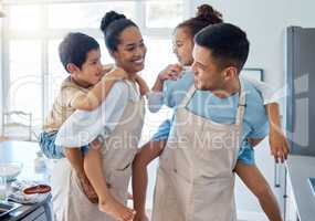 Energetic parents giving their children a piggyback ride while wearing aprons and baking in the kitchen. Hispanic mom and dad playing with kids at home