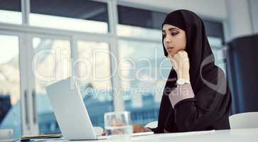 Shes young and ambitious. an attractive young arabic businesswoman working on her laptop in the office.