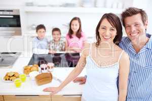 Keeping our family healthy, body and mind. A blissful couple standing alongside a wholesome breakfast with their children blurred in the background.