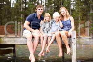 Lakeside family fun. Cute young family sitting together with a smile on a jetty by the lake - portrait.