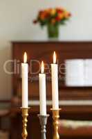 Burning candles in a cosy room against a blurry background. Lighting a candle symbolizes hope and faith in religion. Candle lights in gold and silver holders, for a wedding, funeral home, or church