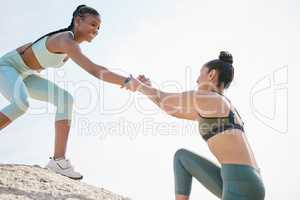 Always ready to lend a helping hand. a woman helping her friend climb a boulder during a workout.