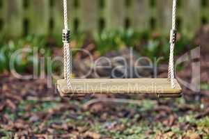 An empty wooden swing in a garden outside in the late afternoon with copyspace. A space to play in a backyard for active children wanting to have fun and play with copy space