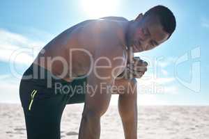 Fit young topless black man taking a break from his run or jog at the beach in the morning for exercise. One strong male bodybuilder athlete looking focused for his cardio and endurance workout