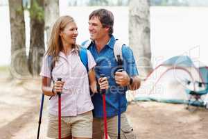 Couple ready for trekking. Happy couple with backpack holding trekking pole and looking at each other.