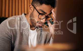 Young stressed indian man or student struggling with headache while browsing on a laptop in a cafe. One tired and frustrated guy suffering with burnout and pressure while studying or working freelance