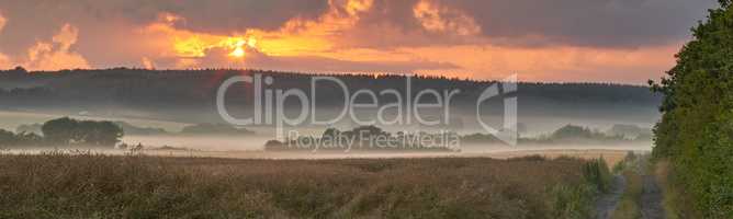 Landscape view of fog over remote field with copy space at sunset. Mist covering a vast expanse of countryside meadow in Germany at dawn. Smoke from wildfire or bush fires rolling over nature reserve