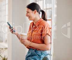 Young happy mixed race businesswoman using her phone while drinking a coffee alone in an office at work. One joyful hispanic businessperson laughing while using social media on her cellphone and holding a coffee cup on a break standing at work