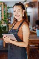 Young hispanic business owner using a wireless tablet in her retail store. Portrait of smiling entrepreneur standing in her restaurant using an online digital device. Young new business owner