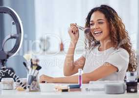 One hispanic woman recording a makeup tutorial for her beauty blog with her phone while sitting at home. African american female influencer live streaming her cosmetic review and recommendation online