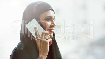 Shes always easy to reach. an attractive young businesswoman dressed in Islamic traditional clothing making a phonecall while standing on her office balcony.