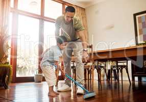 Father pointing to show dust and dirt on wooden floor for son to sweep with broom for household chores at home. Cute boy helping dad with daily spring cleaning tasks. Kid learning to be responsible