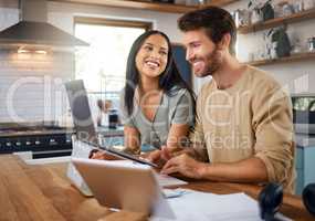 Happy young caucasian man working on laptop in the kitchen at home while his wife stands next to him and smiles while he looks at screen. Happy young interracial couple surfing the internet and enjoying work from home