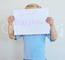Little girl holding a paper with message that bullying at school must be stopped. Blonde child actively protest against bullying, kid starting an anti bully campaign against white copyspace background
