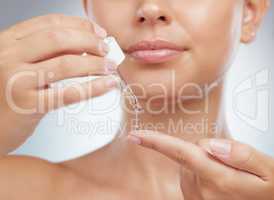 Closeup of unknown woman using dropper to put face serum on a finger. Caucasian model isolated against grey studio background getting ready to use skin oil for healthy glowing skin, skincare routine