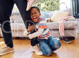 Hes having a bad day. a little boy throwing a tantrum while holding his parents leg at home.