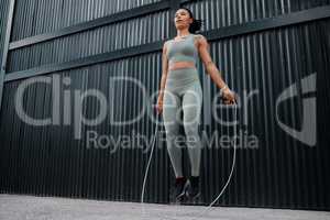 One young african american female athlete skipping using jump rope while exercising outside in the city. Beautiful and dedicated mixed race sportswoman working out alone against an urban background