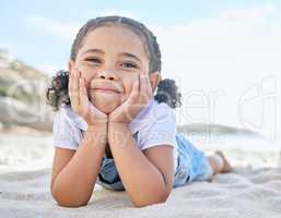 Portrait of one adorable little playful girl relaxing with her hands on her face on a mat at the beach shore. Cheerful cute innocent latino girl smiling while having fun on a summer vacation