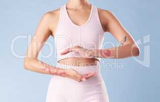 Closeup mixed race fitness woman gesturing around her tummy in studio against a blue background. Young hispanic female athlete with hands placed around her stomach. A good diet promotes gut health