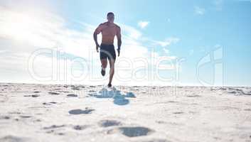 Fit young black man running and jogging on sand at the beach in the morning for exercise. One strong male bodybuilder athlete with six pack abs doing cardio workout to build muscle and endurance