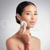 Studio Portrait of a beautiful mixed race woman using a cotton pad to remove makeup during a selfcare grooming routine. Hispanic woman applying cleanser to her face against grey copyspace background