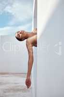 One mixed race woman sitting outside, posing nude on a white structure. Alluring hispanic model hiding her naked body behind a wall. Sensual nudist seductive and free while doing a concept shot