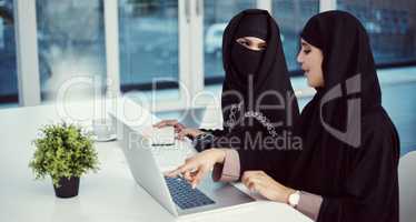 They enjoy working together. two young arabic businesswomen working on a laptop in their office.