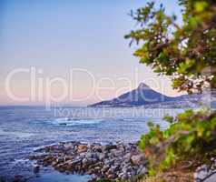 Ocean view on a shallow rocky shoreline with Lions Head, Table Mountain National Park in Cape Town, South Africa in the background. Quiet calm beach during sunset on a beautiful summer evening