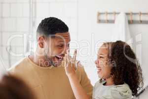 Happy mixed race father and daughter washing their hands together in a bathroom at home. Single African American parent teaching his daughter about hygiene while having fun and being playful