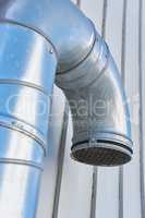 Closeup of a large metal ventilation pipe against the side of a building outside. Engineered stainless steel extractor fan system for fresh air. Galvanized structure for clean, healthy air and oxygen