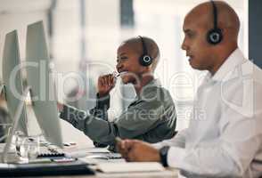 Happy young african american call centre telemarketing agent talking on a headset while working on a computer in an office alongside a colleague. Confident friendly female consultant operating helpdesk for customer service and sales support