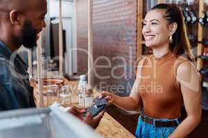 Happy hispanic customer paying for a meal in a restaurant using a nfc machine and credit card. Smiling young woman making a purchase in a store with her debit card and a pos machine. Woman paying bill