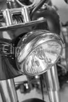 Closeup front view of a head light on a motorbike. A monochrome vintage motorcycle in black and white. One modern silver chrome transportation vehicle. Maintenance on a classic retro custom bike