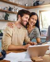 Beautiful young wife standing behind her husband working on his laptop while they look at the screen together and smile. Happy young interracial couple surfing the internet and enjoying work from home