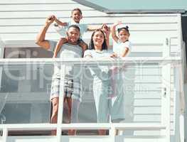 Portrait of happy mixed race family with two children wearing pyjamas and smiling and waving at camera while standing on balcony at their new house or while on holiday