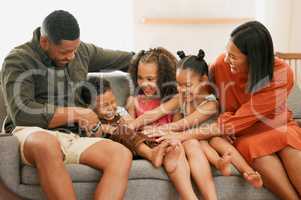 A happy mixed race family of five relaxing on the sofa at home. Loving black family being playful on the sofa. Young couple bonding with their foster kids at home