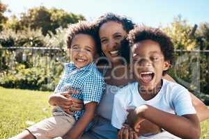 Excited little boy with afro sitting outside on the grass with his mother and brother. Energetic african american family spending time outdoors at the park or their backyard. Mom embracing two sons