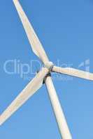 Closeup of a wind turbine and propellor blades against a blue sky background from below. Harvesting a sustainable and renewable source of energy to generate power and electricity from windy climates