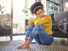 Young unhappy mixed race woman looking sad and thinking while wearing headphones and listening to music alone at home. One hispanic woman looking depressed and going through a breakup at home