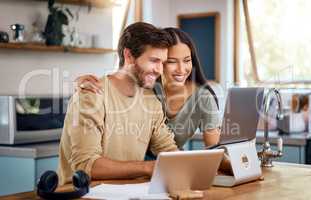 Beautiful young hispanic wife standing behind her caucasian husband working on his laptop while they look at the screen together and smile. Happy young interracial couple surfing the internet, looking at home finances and enjoying work from home