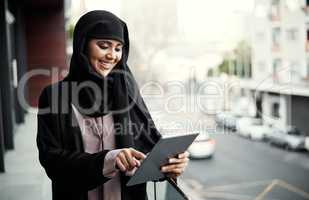 Work smart, not hard. an attractive young businesswoman dressed in Islamic traditional clothing using a tablet while standing on her office balcony.